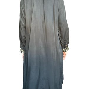 May include: A long-sleeved black duster coat featuring a subtle ombre effect that transitions to a darker shade at the hem. The garment includes long sleeves with decorative cuffs adorned with intricate gold and black beaded embroidery details.