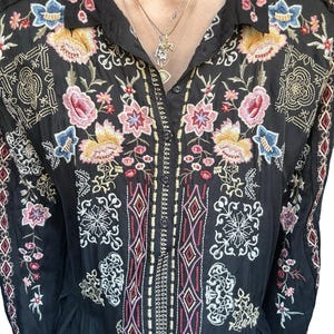 May include: A black long-sleeved button-down shirt featuring intricate multi-colored floral and geometric embroidery in shades of pink, yellow, blue, and white across the chest, shoulders, and sleeves, with a classic collar and front button placket.