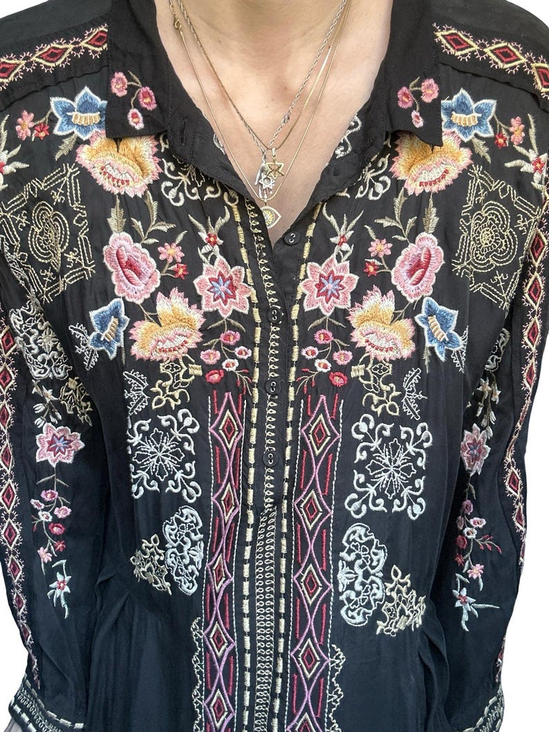 May include: A black long-sleeved button-down shirt featuring intricate multi-colored floral and geometric embroidery in shades of pink, yellow, blue, and white across the chest, shoulders, and sleeves, with a classic collar and front button placket.