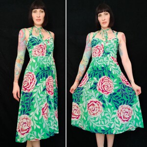 May include: A green halter dress with a floral pattern featuring large pink roses, white leaves, and blue accents. The dress has a fitted bodice and a flowing skirt. The dress is made of a lightweight fabric.