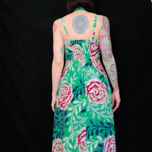 May include: A green floral print dress with a halter neckline and spaghetti straps. The dress features large pink and white peony-like flowers and blue leaves on a green background. The dress is knee-length.