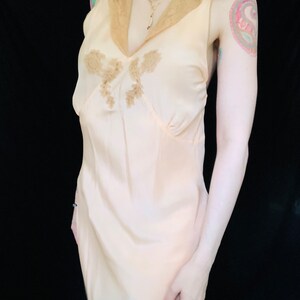 May include: A pale pink silk slip dress with a lace trim collar and delicate floral embroidery. The dress has a fitted bodice and a flowing skirt.