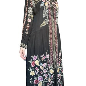 May include: A black long-sleeved dress featuring a vibrant floral embroidery pattern in shades of pink, purple, yellow, and white. The garment includes a central vertical panel with geometric diamond motifs and a collared neckline with a V-shaped opening.