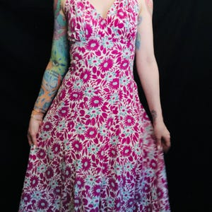May include: A pink and white floral print halter dress with a V-neckline. The dress has a fitted bodice and a flowing skirt.