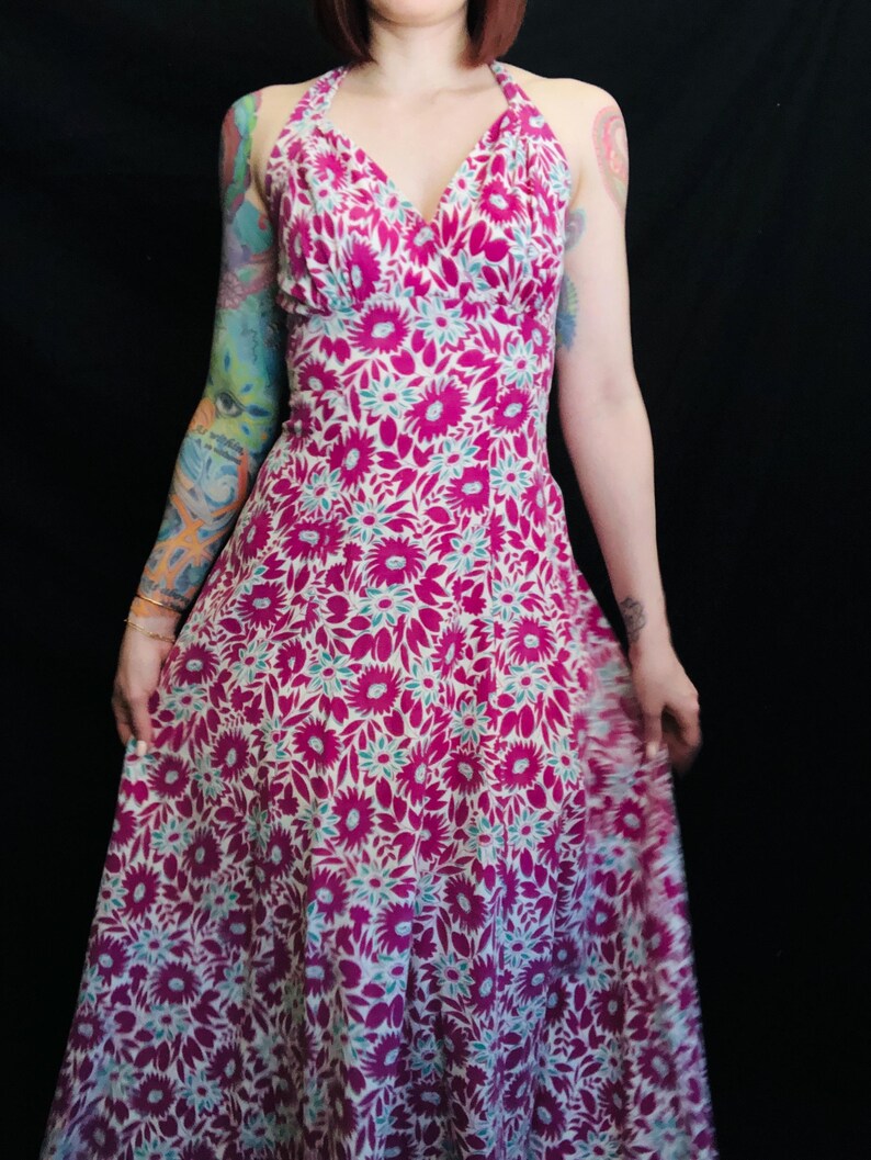 May include: A pink and white floral print halter dress with a V-neckline. The dress has a fitted bodice and a flowing skirt.