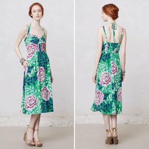 May include: A green halter dress with a floral pattern featuring large pink and white roses, blue accents, and green leaves. The dress has a knee-length skirt and a fitted bodice. The dress is shown from the front and back.
