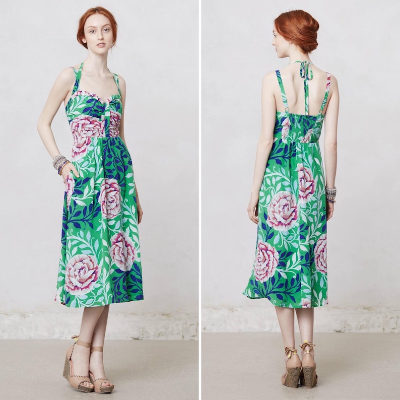 May include: A green halter dress with a floral pattern featuring large pink and white roses, blue accents, and green leaves. The dress has a knee-length skirt and a fitted bodice. The dress is shown from the front and back.
