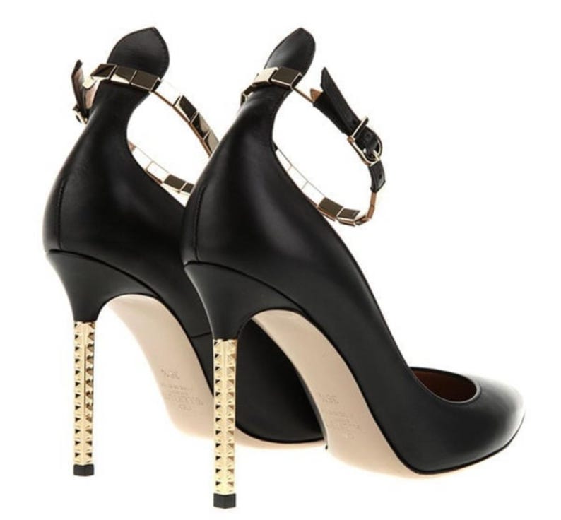 May include: Black leather high heels with gold-tone studded heels and ankle straps. The shoes have a pointed toe and a gold-tone buckle closure. The heels are approximately 4 inches tall.