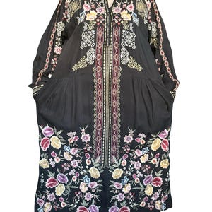 May include: A black long-sleeved dress featuring a central vertical panel with geometric patterns and colorful floral embroidery at the hem and shoulders. The garment has a button-down collar, long sleeves, and a loose, flowing silhouette.