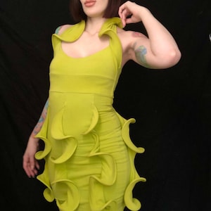 May include: A lime green halter dress with a fitted bodice and a flared skirt. The dress features decorative, curved fabric accents along the skirt and neckline. The dress is made of a stretchy material and is knee-length.