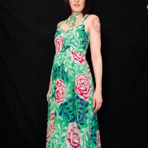 May include: A green floral print dress with a halter neckline and a flowing skirt. The dress features large pink and white flowers with blue and white foliage against a bright green background. The dress is sleeveless and appears to be made of a lightweight fabric.