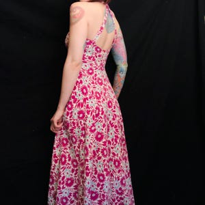 May include: A pink and white floral maxi dress with a halter neckline and a fitted bodice. The dress has a flowing skirt and is made of a lightweight fabric.