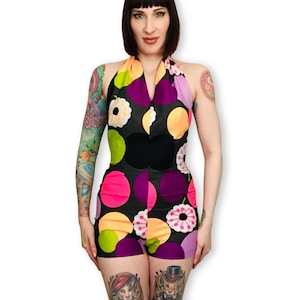 Può includere: Un body con collo all'americana con sfondo nero e grandi pois colorati in rosa, viola, arancione e verde. Il body ha un corpetto e pantaloncini neri. Il top all'americana presenta un motivo floreale.