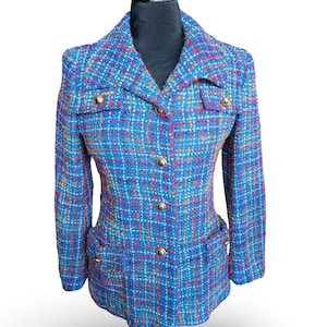 May include: A blue tweed jacket with a multi-colored plaid pattern. The jacket has a notched collar, two front pockets, and gold-colored buttons. The jacket is displayed on a black mannequin.