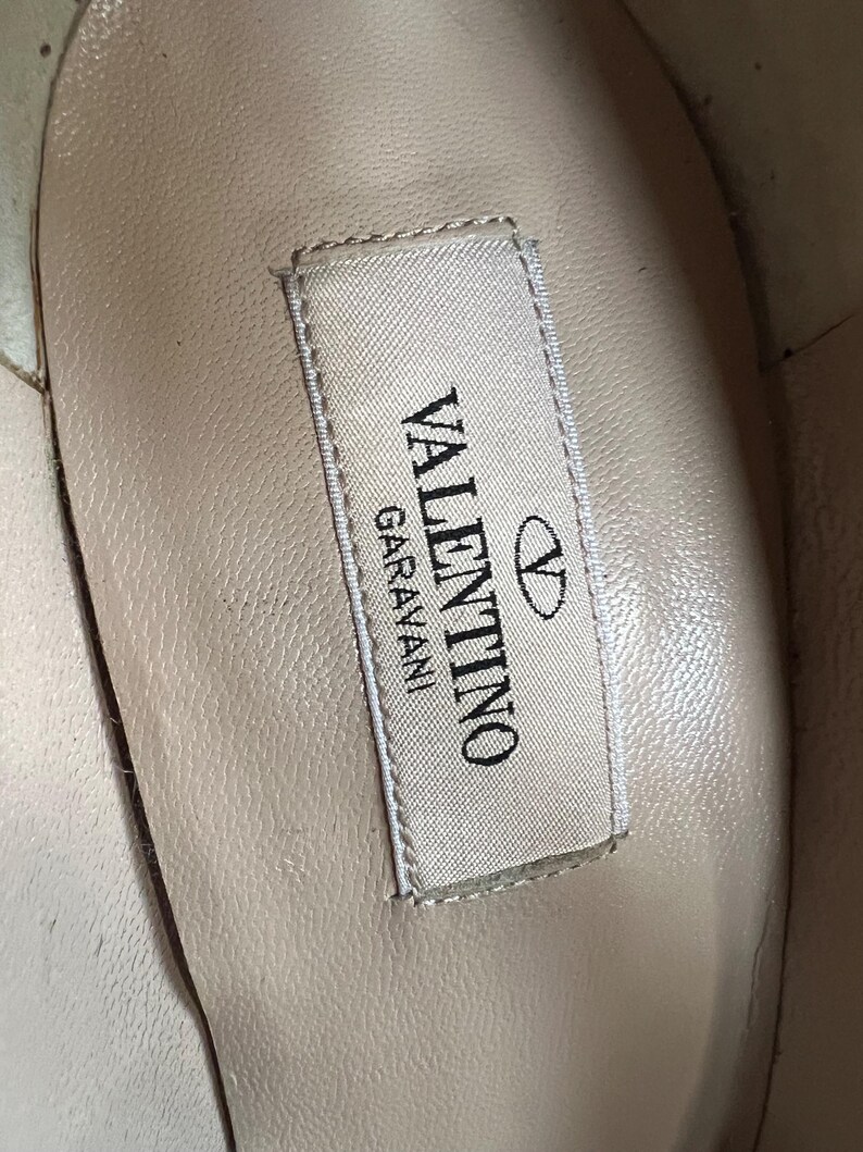 May include: Close-up of the interior of a shoe, showcasing a label with the brand name "VALENTINO GARAVANI" in black text. The label is rectangular with a white background and a silver border. The Valentino logo is also visible.