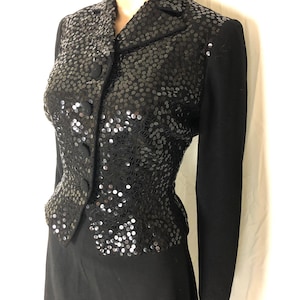 May include: A black sequined jacket with a fitted silhouette and a button-up front. The jacket has long sleeves and a collar.
