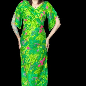 May include: A floor-length dress featuring a vibrant green botanical print with bright pink floral accents. The garment has a V-neckline, a gathered crossover bodice, and short, split-sleeve details that extend from the shoulders.