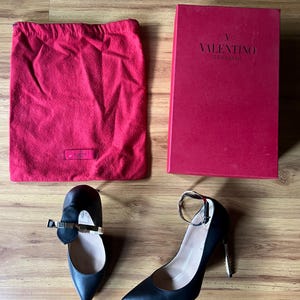 May include: Black leather high heels and flats with gold accents, a red dust bag, and a red Valentino Garavani box. The shoes have pointed toes and ankle straps. The box has the Valentino Garavani logo.