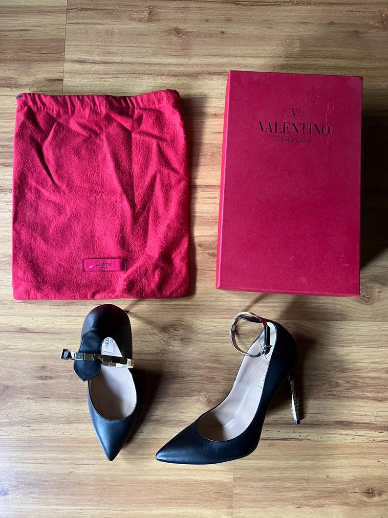 May include: Black leather high heels and flats with gold accents, a red dust bag, and a red Valentino Garavani box. The shoes have pointed toes and ankle straps. The box has the Valentino Garavani logo.