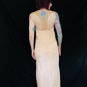 May include: A long, pale pink slip dress with a lace back. The dress has a simple, elegant design and is perfect for a special occasion.