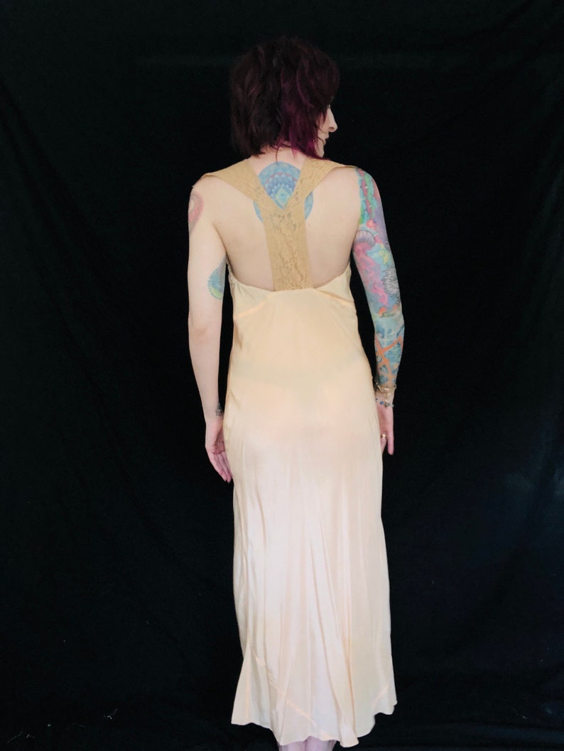 May include: A long, pale pink slip dress with a lace back. The dress has a simple, elegant design and is perfect for a special occasion.