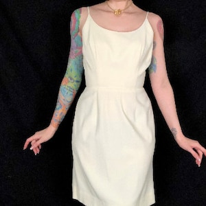 May include: A white sleeveless dress with a scoop neck and a fitted silhouette. The dress has a simple design and is made of a smooth fabric.