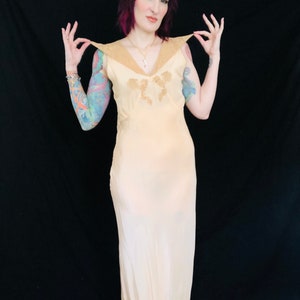 May include: A pale yellow silk slip dress with a lace trim and a V-neckline. The dress has a fitted bodice and a flowing skirt.