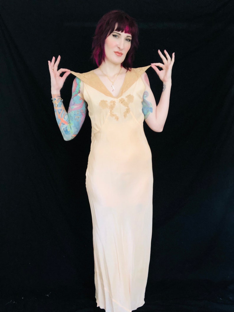May include: A pale yellow silk slip dress with a lace trim and a V-neckline. The dress has a fitted bodice and a flowing skirt.