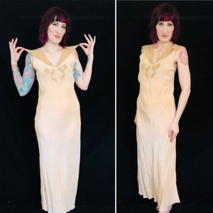 May include: A long, sleeveless, peach-colored slip dress with a lace trim and a delicate floral design. The dress has a V-neckline and a flowing silhouette.