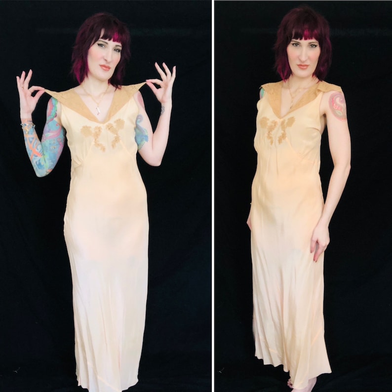 May include: A long, sleeveless, peach-colored slip dress with a lace trim and a delicate floral design. The dress has a V-neckline and a flowing silhouette.