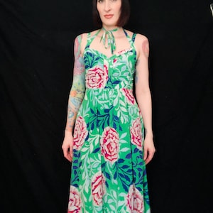 May include: A green floral print dress with a halter neckline and a knee-length skirt. The dress features a pattern of large pink roses, blue leaves, and white foliage. The background is black.