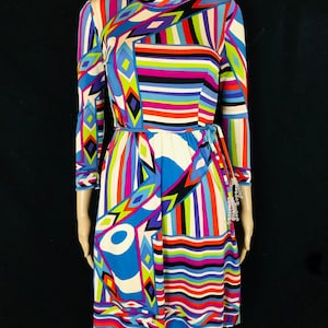 May include: A colorful, geometric patterned dress with long sleeves and a tie at the waist. The dress is made of a silky fabric and has a vibrant, abstract design.