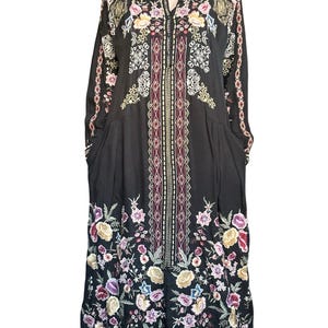 May include: A black long-sleeved midi dress featuring a central vertical panel with geometric patterns and colorful floral embroidery. The garment includes a button-down front, a collar, and intricate flower motifs in shades of pink, yellow, and blue.