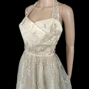 May include: A white halter dress with a full skirt and a sequined bodice. The dress is made of tulle and has a vintage style.