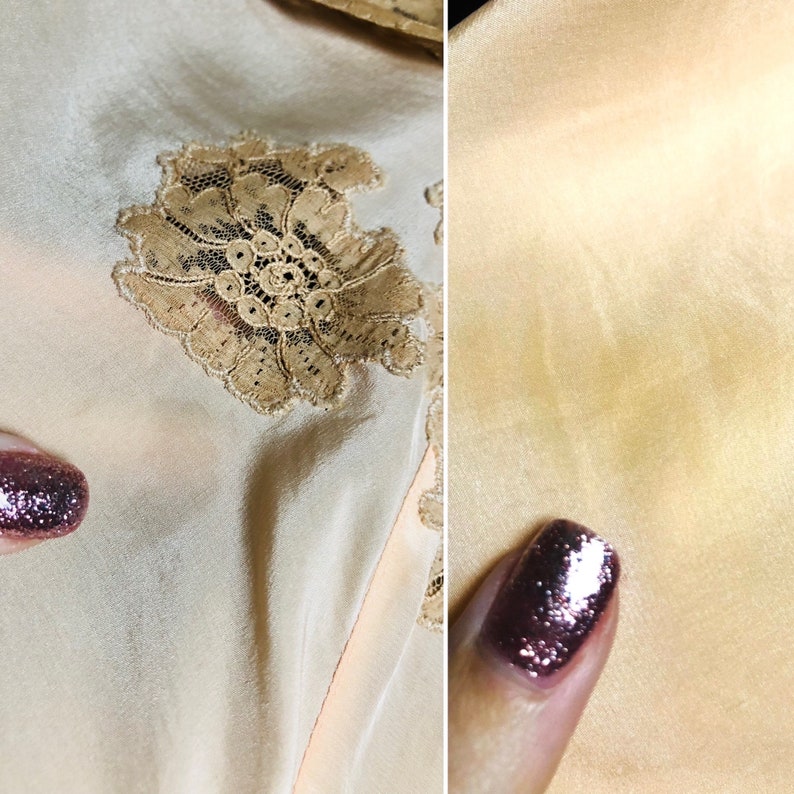 May include: Close-up of a pale peach colored fabric with a delicate lace floral design. The fabric has a subtle sheen and a smooth texture.