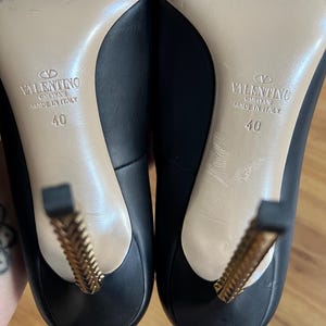 May include: A pair of black leather high heels with gold-colored decorative heels. The soles are beige, and the shoes are marked "VALENTINO GARAVANI MADE IN ITALY" with a size 40.