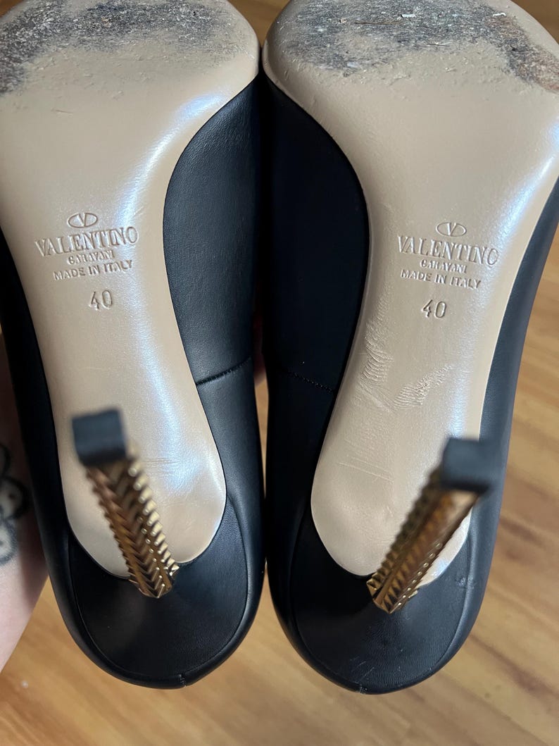 May include: A pair of black leather high heels with gold-colored decorative heels. The soles are beige, and the shoes are marked "VALENTINO GARAVANI MADE IN ITALY" with a size 40.