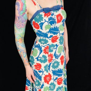 May include: A white maxi dress with a blue, green, and red floral print. The dress has a fitted bodice and a flowy skirt. The straps are thin and adjustable.