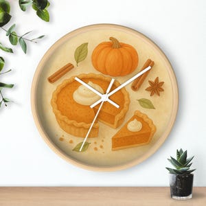 Op de afbeelding: Ronde wandklok met een licht houten frame. De wijzerplaat toont een pompoentaart, een hele pompoen, kaneelstokjes en steranijs. De wijzers van de klok zijn wit.
