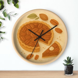 May include: Circular wall clock with a pecan pie design. The clock face depicts a detailed illustration of a pecan pie with a slice removed. The clock has a light wood frame and black hands. The color scheme is warm browns and tans, with measurements in centimetres.