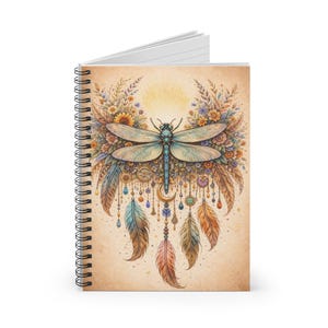 May include: Spiral-bound notebook featuring a detailed illustration of a dragonfly with outstretched wings, surrounded by flowers, feathers, and dangling beads. The design has a vintage, bohemian aesthetic with a warm color palette.
