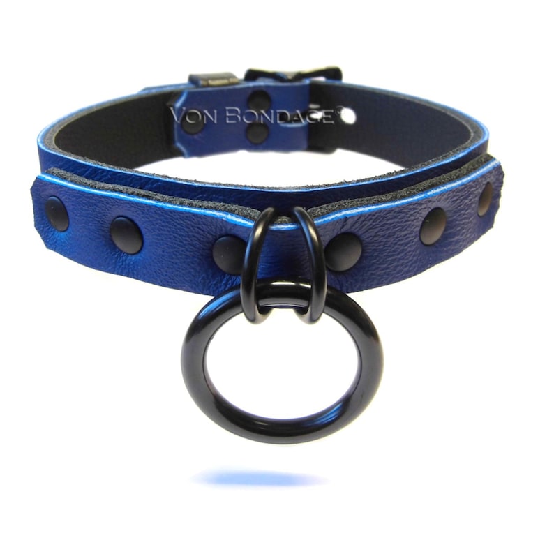May include: A blue leather collar with black hardware, including a large ring and buckle. The collar is riveted and features the text "Von Bondage".