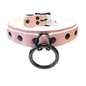 May include: A pink leather collar with black hardware and a large black O-ring. The collar has black rivets and a white interior lining. The text "VON BONDAGE" is visible on the collar.