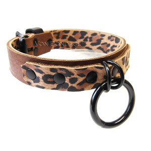May include: A brown leather collar with a leopard print pattern. The collar has black hardware, including a buckle, rivets, and a large ring. The text "VON BONDAGE" is visible on the collar.