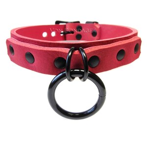 May include: A red collar with black hardware and a large black ring. The collar has black rivets and the text "Von Bondage".