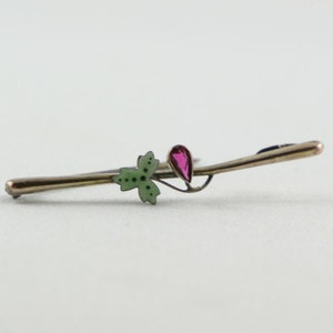 Puede incluir: Un broche de plata y oro con una hoja de esmalte verde y una piedra de cristal roja.