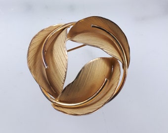 May include: A gold-toned brooch featuring a design of overlapping leaves.