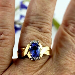 May include: A gold ring with a blue oval gemstone surrounded by smaller diamonds. The ring has a twisted band.