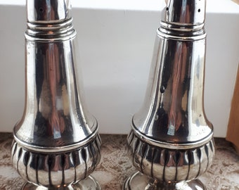 May include: A pair of silver salt shakers with a fluted design and a domed top. The shakers have a polished finish and are in good condition.