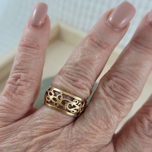 Op de afbeelding: Een gouden filigraanring met een delicaat, ingewikkeld ontwerp. De ring wordt aan een vinger gedragen.